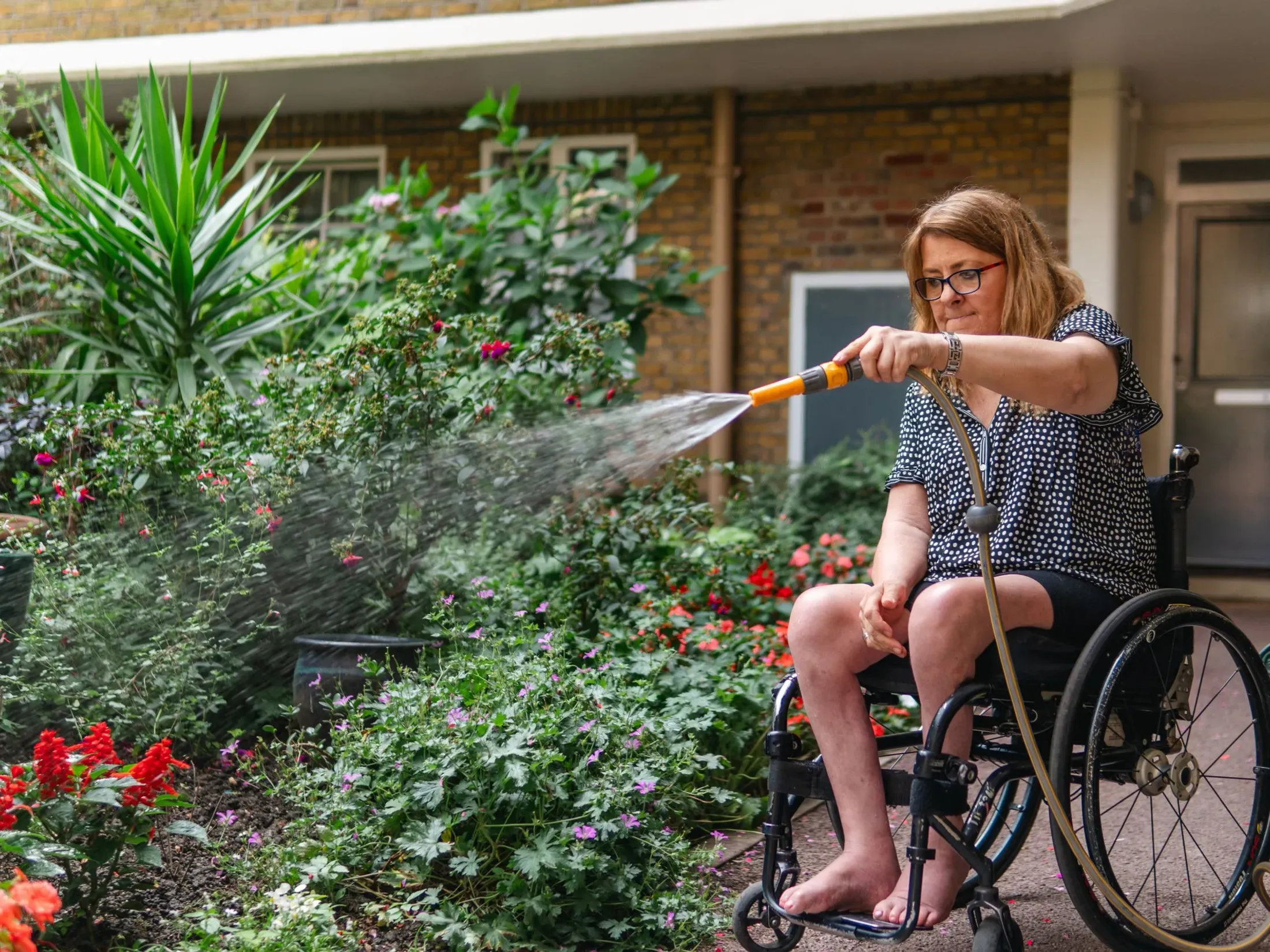 A woman watering a lush flower garden from her wheelchair