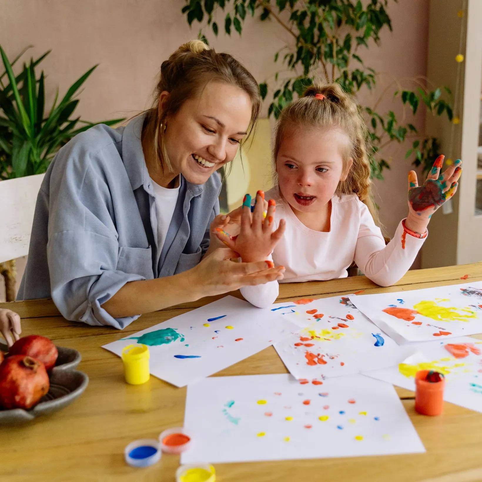 A support worker and a young girl finger painting together at a kitchen table